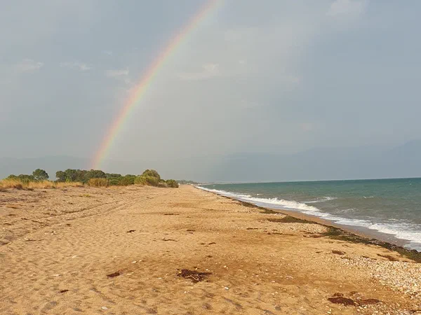 Rainbow above the sandy beach, the sea on the right