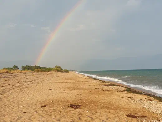 Regenbogen über dem Sandstrand, rechts das Meer