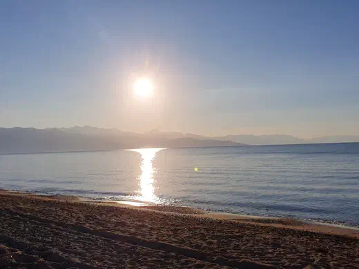 Sonne über dem Meer, vom Strand aus gesehen, dahinter eine Bergkette