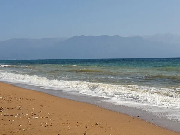 Waves running onto a sandy beach, a hazy mountain range behind