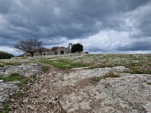 Stone chapel on a hill under dark clouds, a flowering meadow all around