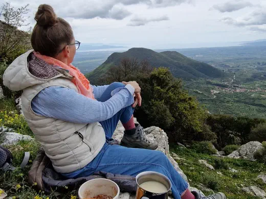 Stefanie sitzt auf einem Felsen und blickt ins Tal, davor das Frühstück auf dem Campingkocher