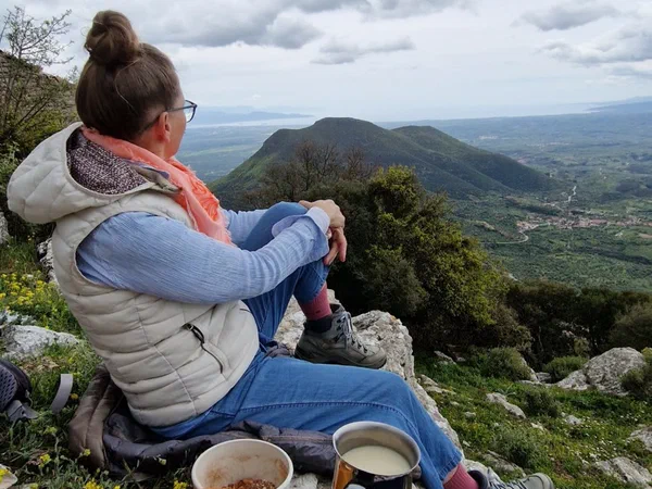 Stefanie sits on a rock looking into the valley, breakfast on the camping stove in front