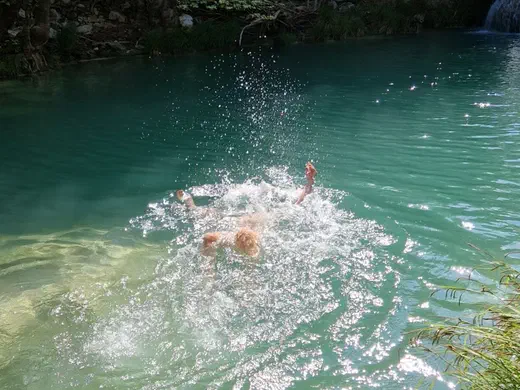 Jemand springt in den türkisfarbenen See, das Wasser spritzt auf