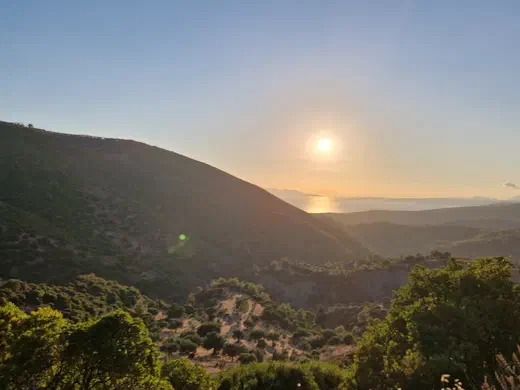 Tief stehende Sonne über dem Meer, gesehen aus einem Tal zwischen Hügeln