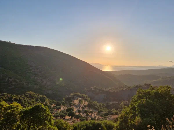 Low sun above the sea, seen from a valley between hills