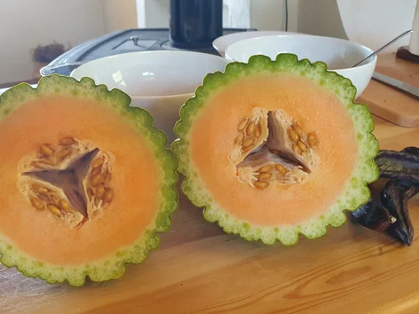 Two melon halves on a wooden table, carob pods beside them