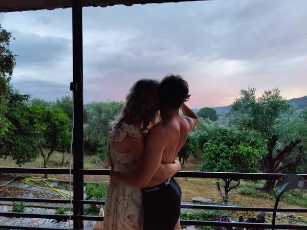 Two young people embrace on the terrace and look out into the dusk