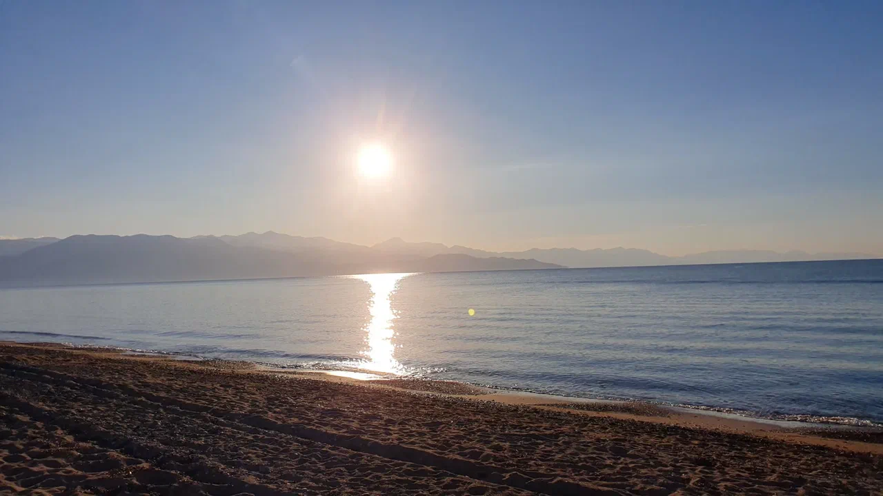 The sun above the sea, seen from the beach, with a mountain range behind it