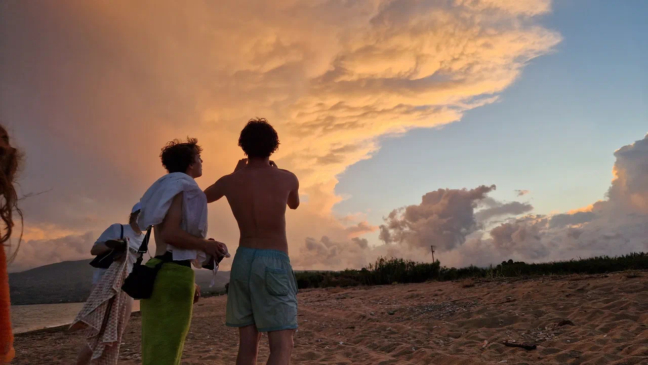 People on the beach look out at tall clouds coloured orange by the evening light
