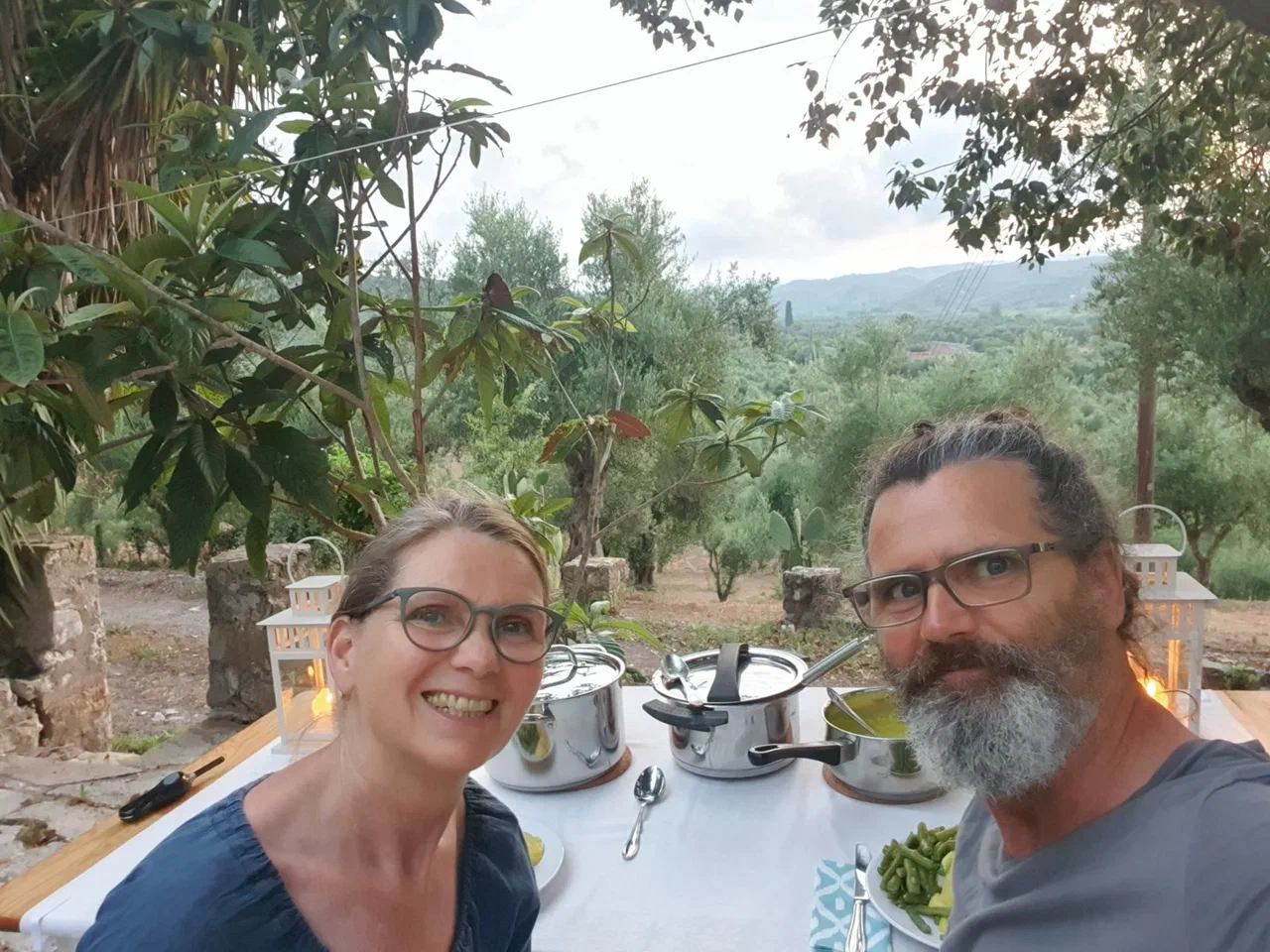 Stefanie und Clemens beim Abendessen an einem gedeckten Tisch im Freien, dahinter Olivenbäume