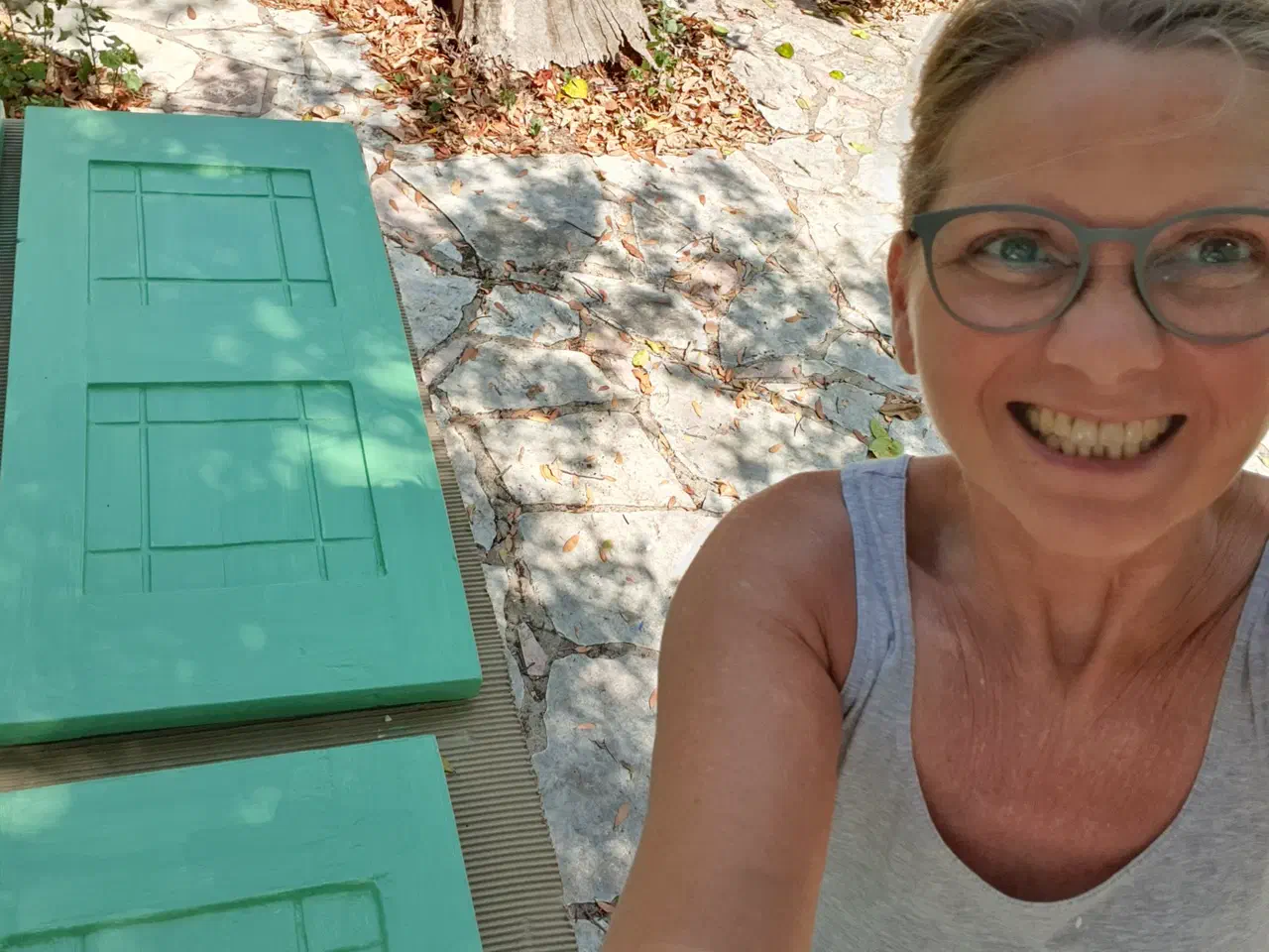 Stefanie beim Streichen von Fensterläden in Türkis, im Schatten eines Baumes